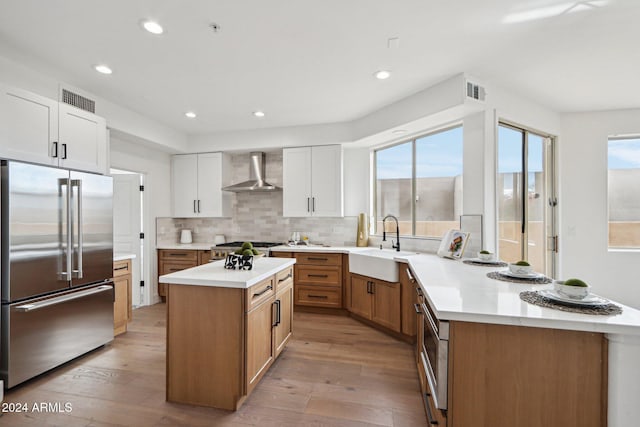 kitchen featuring appliances with stainless steel finishes, wall chimney exhaust hood, sink, a center island, and white cabinetry