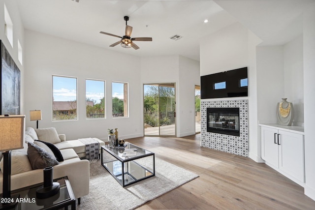 living room featuring a tile fireplace, ceiling fan, plenty of natural light, and light hardwood / wood-style floors