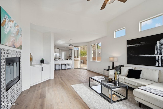 living room featuring light wood-type flooring, ceiling fan, and a tiled fireplace