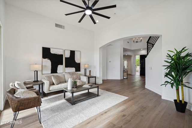 living room featuring a towering ceiling, wood-type flooring, and ceiling fan with notable chandelier