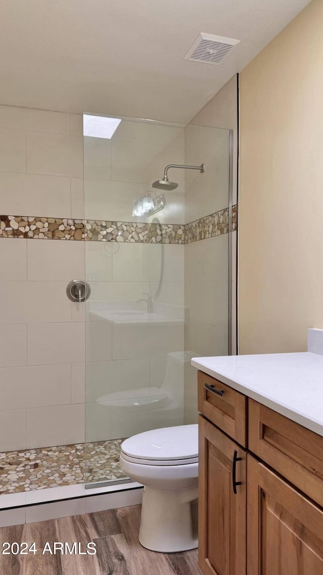 bathroom featuring vanity, hardwood / wood-style floors, toilet, and tiled shower