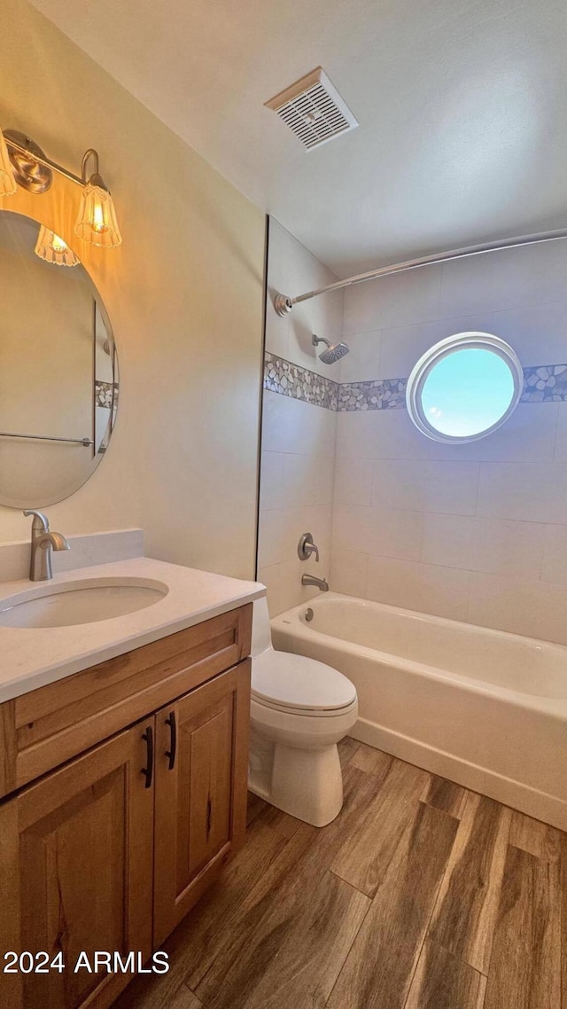 full bathroom featuring wood-type flooring, vanity, tiled shower / bath combo, and toilet