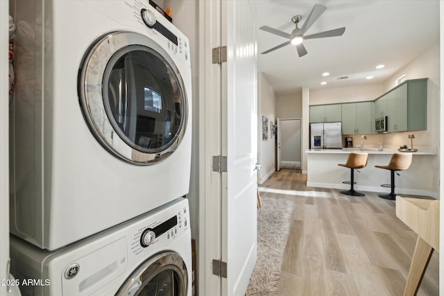 laundry room with stacked washer / dryer, ceiling fan, sink, and light wood-type flooring