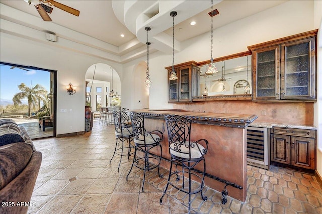 bar featuring ceiling fan, pendant lighting, decorative backsplash, a towering ceiling, and beverage cooler