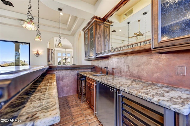 bar with decorative light fixtures, refrigerator, sink, light tile patterned floors, and light stone counters