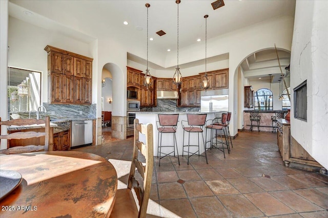 kitchen featuring decorative light fixtures, a wealth of natural light, built in appliances, and tasteful backsplash