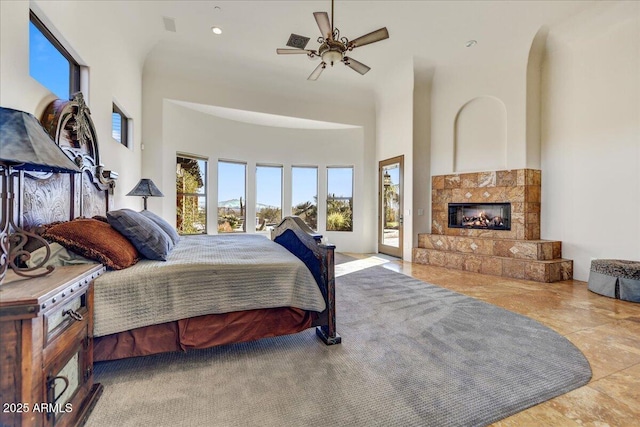 bedroom with ceiling fan, access to exterior, a fireplace, and a towering ceiling