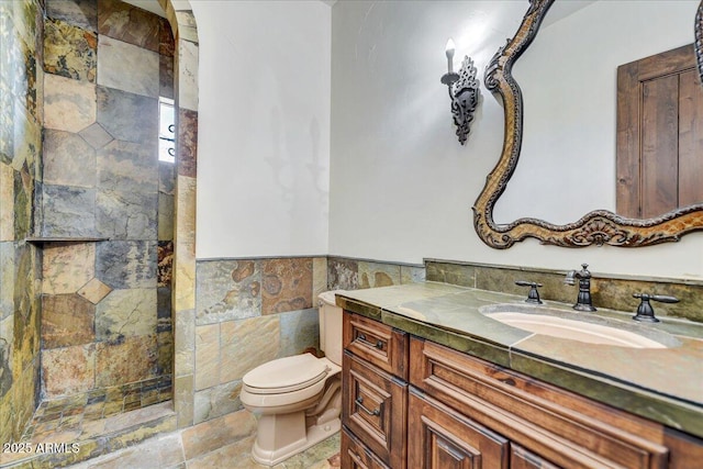 bathroom with toilet, vanity, tile walls, and walk in shower