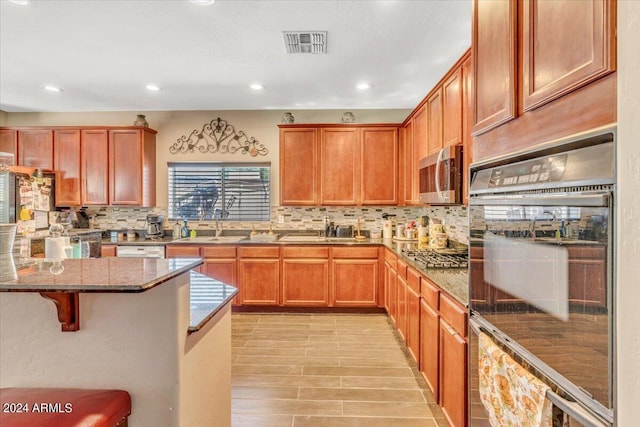 kitchen featuring a kitchen bar, appliances with stainless steel finishes, stone countertops, and tasteful backsplash