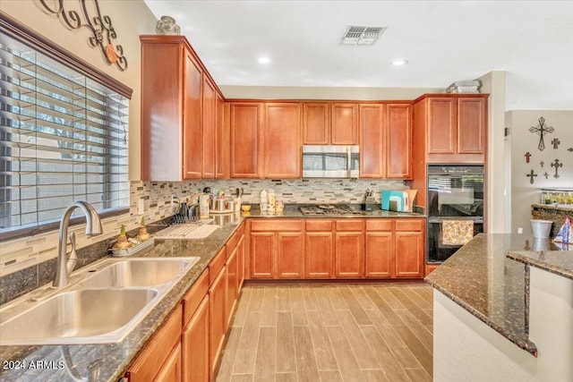 kitchen with dark stone counters, sink, decorative backsplash, light wood-type flooring, and appliances with stainless steel finishes