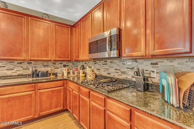 kitchen with decorative backsplash, appliances with stainless steel finishes, light wood-type flooring, and dark stone counters