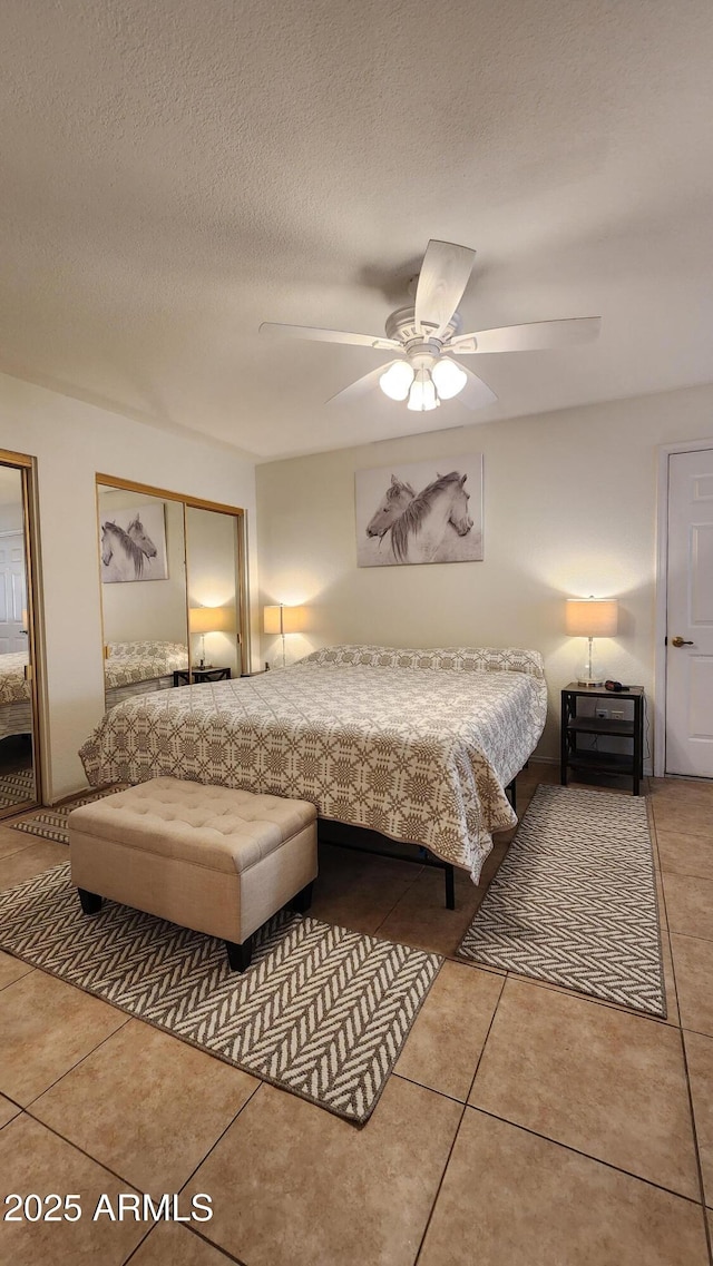 bedroom with ceiling fan, two closets, a textured ceiling, and light tile patterned flooring