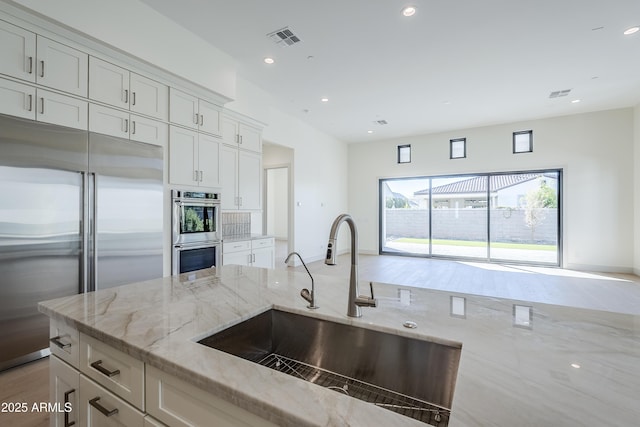kitchen featuring a sink, appliances with stainless steel finishes, light stone counters, white cabinets, and recessed lighting