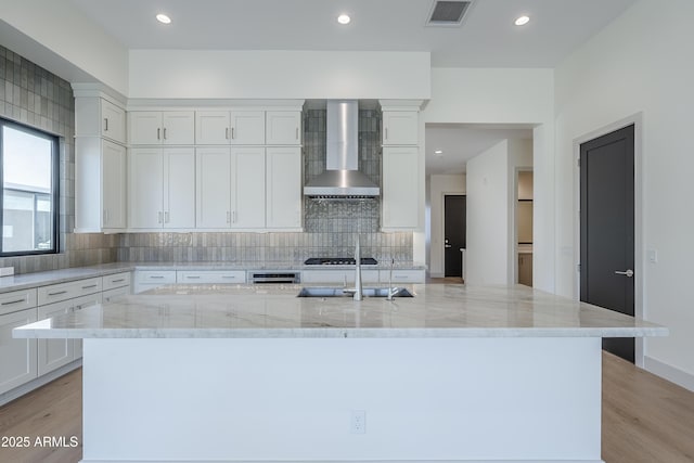 kitchen with wall chimney range hood, a sink, decorative backsplash, white cabinetry, and recessed lighting