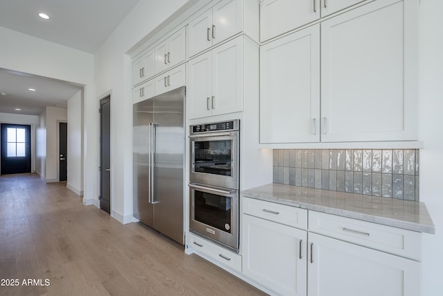 kitchen with stainless steel appliances, light stone counters, light wood finished floors, white cabinets, and recessed lighting