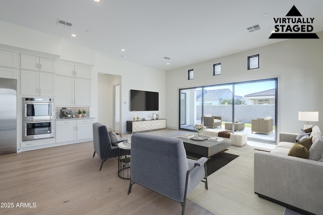 living area with light wood-type flooring, a high ceiling, and recessed lighting
