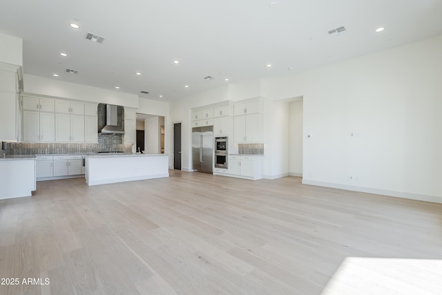 unfurnished living room with recessed lighting, light wood finished floors, a sink, and baseboards