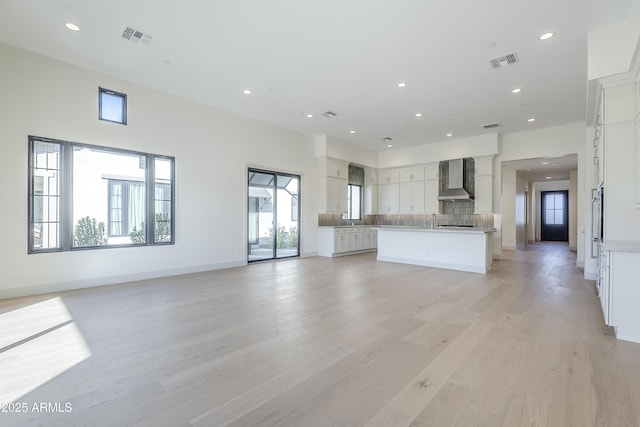 unfurnished living room featuring ornate columns, light wood-style flooring, recessed lighting, a sink, and baseboards