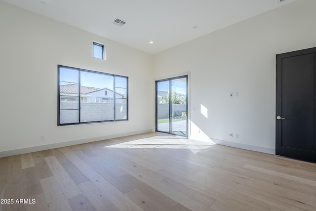 empty room with plenty of natural light, light wood finished floors, baseboards, recessed lighting, and a towering ceiling