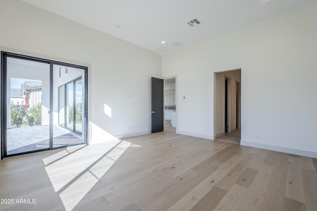unfurnished room with light wood-style floors, baseboards, and a high ceiling