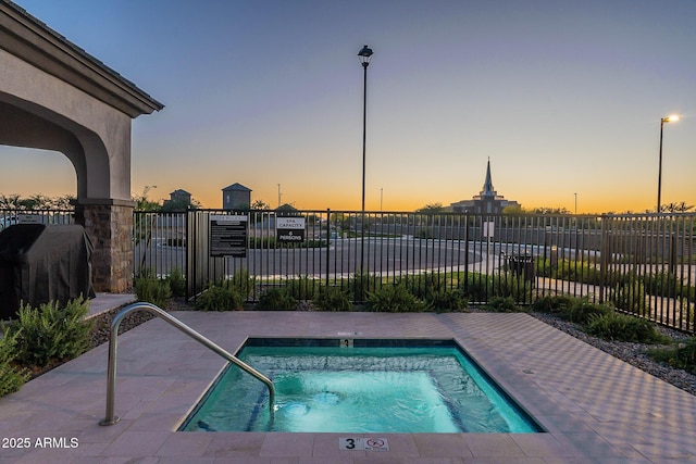 pool at dusk with fence, a swimming pool, and area for grilling