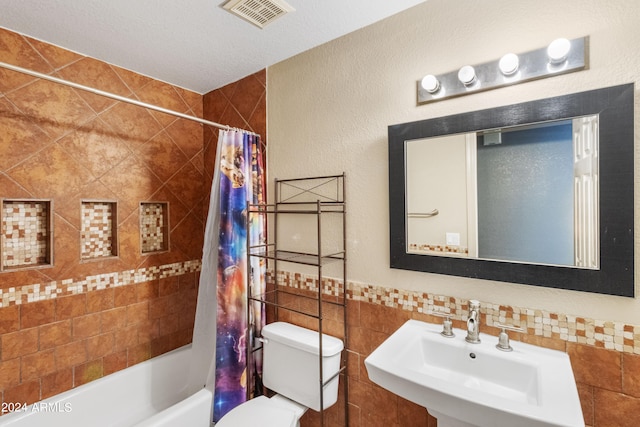 full bathroom with tile walls, shower / tub combo, a textured ceiling, toilet, and sink