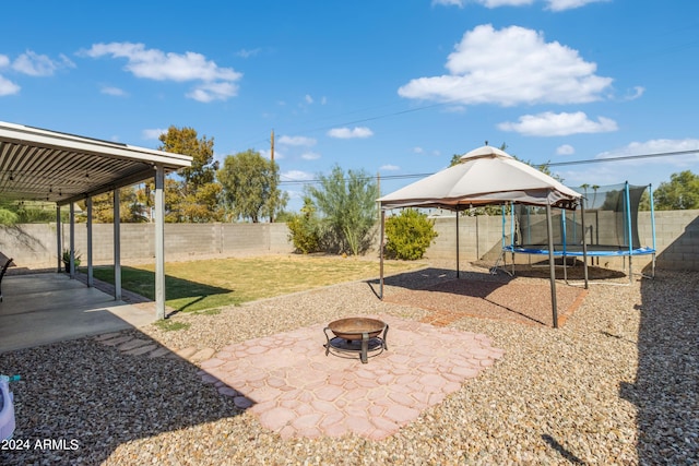 view of yard featuring a trampoline, a patio area, and an outdoor fire pit