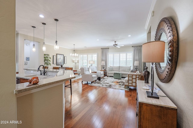 living room featuring wood-type flooring, ceiling fan with notable chandelier, ornamental molding, and sink