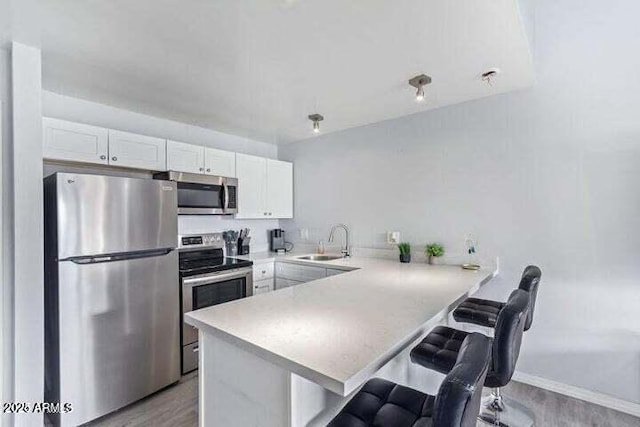 kitchen featuring a breakfast bar area, appliances with stainless steel finishes, a sink, light countertops, and white cabinets