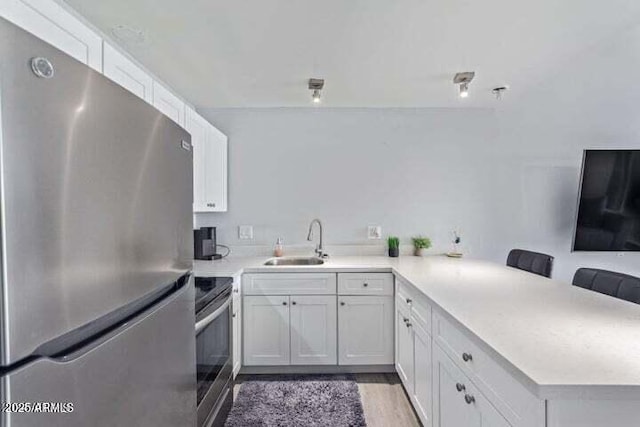 kitchen featuring a peninsula, light countertops, white cabinets, a sink, and stainless steel appliances