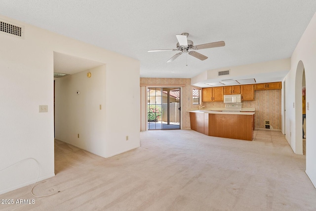 kitchen with visible vents, white microwave, brown cabinetry, open floor plan, and a peninsula