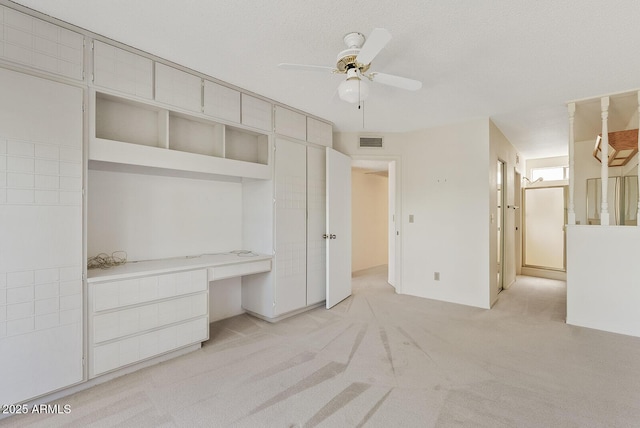 unfurnished bedroom featuring ceiling fan, a textured ceiling, light carpet, visible vents, and built in desk