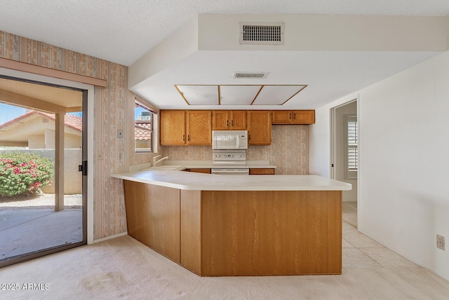 kitchen with light countertops, visible vents, a sink, white appliances, and a peninsula