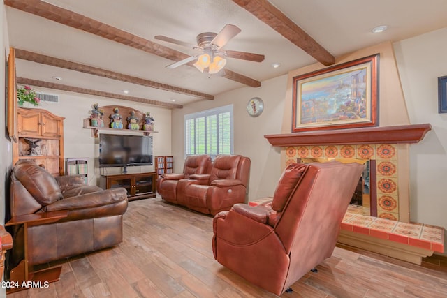 living room with beamed ceiling, a tiled fireplace, ceiling fan, and light wood-type flooring