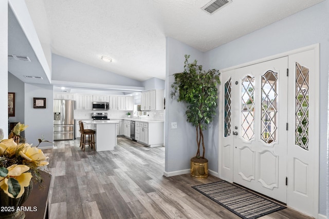foyer entrance featuring lofted ceiling, light wood-type flooring, baseboards, and a textured ceiling