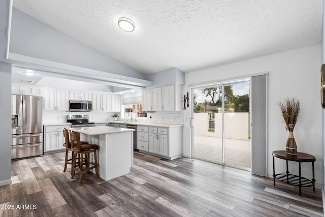 kitchen featuring stainless steel appliances, vaulted ceiling, backsplash, a textured ceiling, and a kitchen island