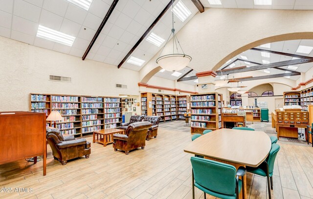 dining room with high vaulted ceiling, wood finished floors, beam ceiling, a textured wall, and arched walkways