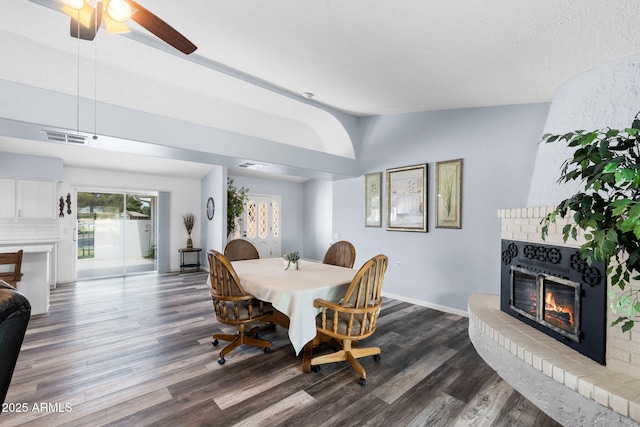dining area featuring a brick fireplace, vaulted ceiling, dark wood-type flooring, baseboards, and a ceiling fan
