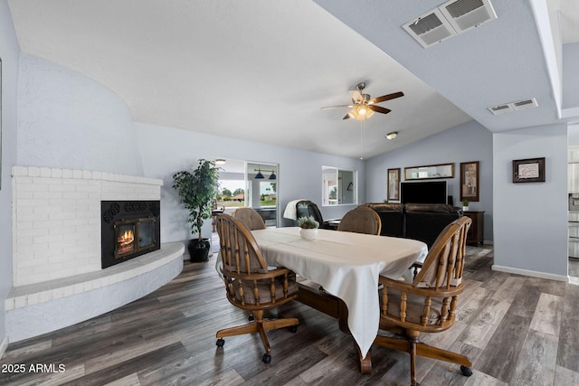 dining room with ceiling fan, lofted ceiling, wood finished floors, a brick fireplace, and baseboards