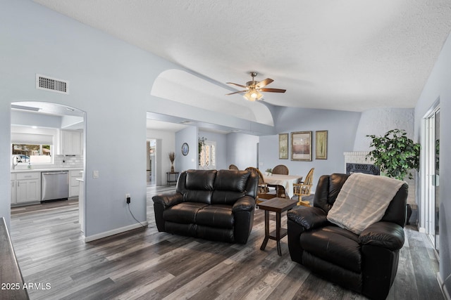living room with wood finished floors, lofted ceiling, a ceiling fan, arched walkways, and a textured ceiling