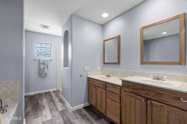 full bath featuring wood finished floors, double vanity, baseboards, and a bath
