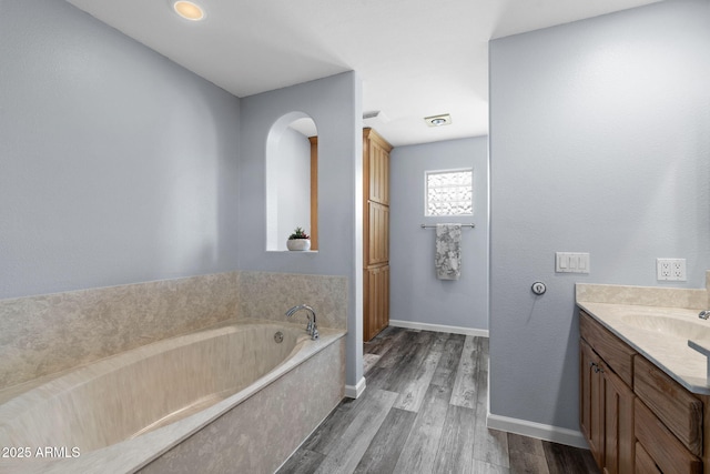 full bathroom featuring wood finished floors, vanity, a bath, and baseboards