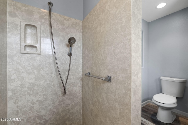 bathroom with wood finished floors, toilet, a tile shower, and baseboards