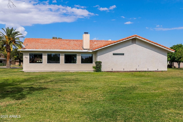 rear view of property featuring a tiled roof, a chimney, a yard, and stucco siding