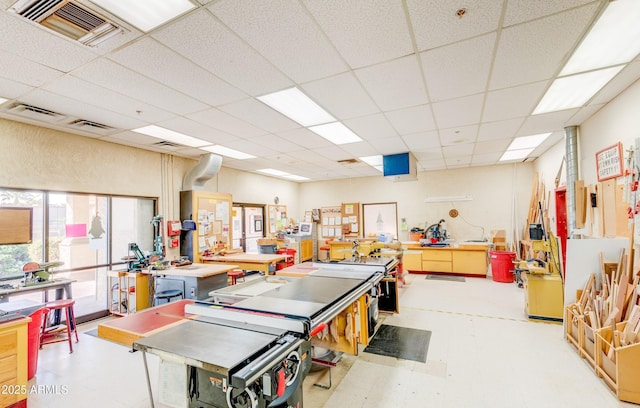 game room with light floors, a workshop area, and a paneled ceiling