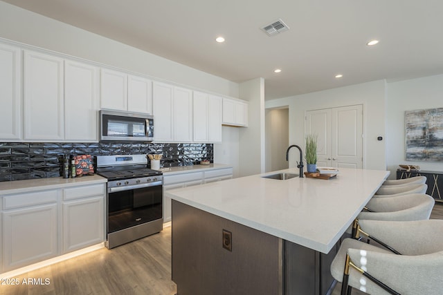 kitchen with a sink, visible vents, white cabinets, appliances with stainless steel finishes, and decorative backsplash