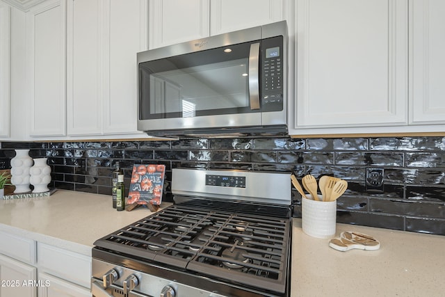 kitchen with stainless steel appliances, backsplash, white cabinetry, and light stone countertops