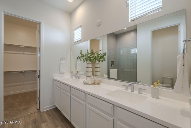 bathroom featuring double vanity, a sink, toilet, and a shower stall