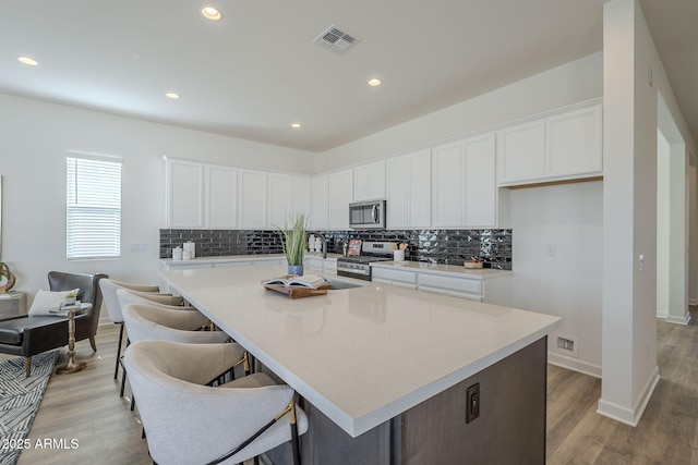 kitchen with appliances with stainless steel finishes, white cabinets, visible vents, and decorative backsplash