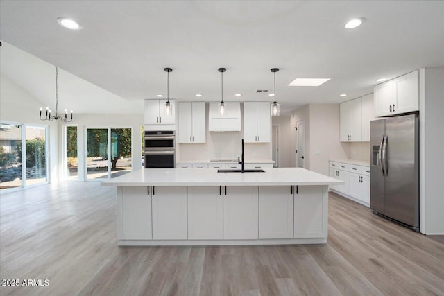 kitchen with an island with sink, appliances with stainless steel finishes, white cabinets, and decorative light fixtures